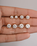 Diamond stud earrings of different sizes held in a hand with measurements indicated.