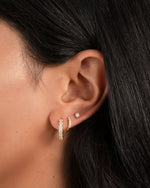 gold cubic zirconia huggie hoop earrings on model, paired with a mini pave hoop earring and a solitaire stud earring
