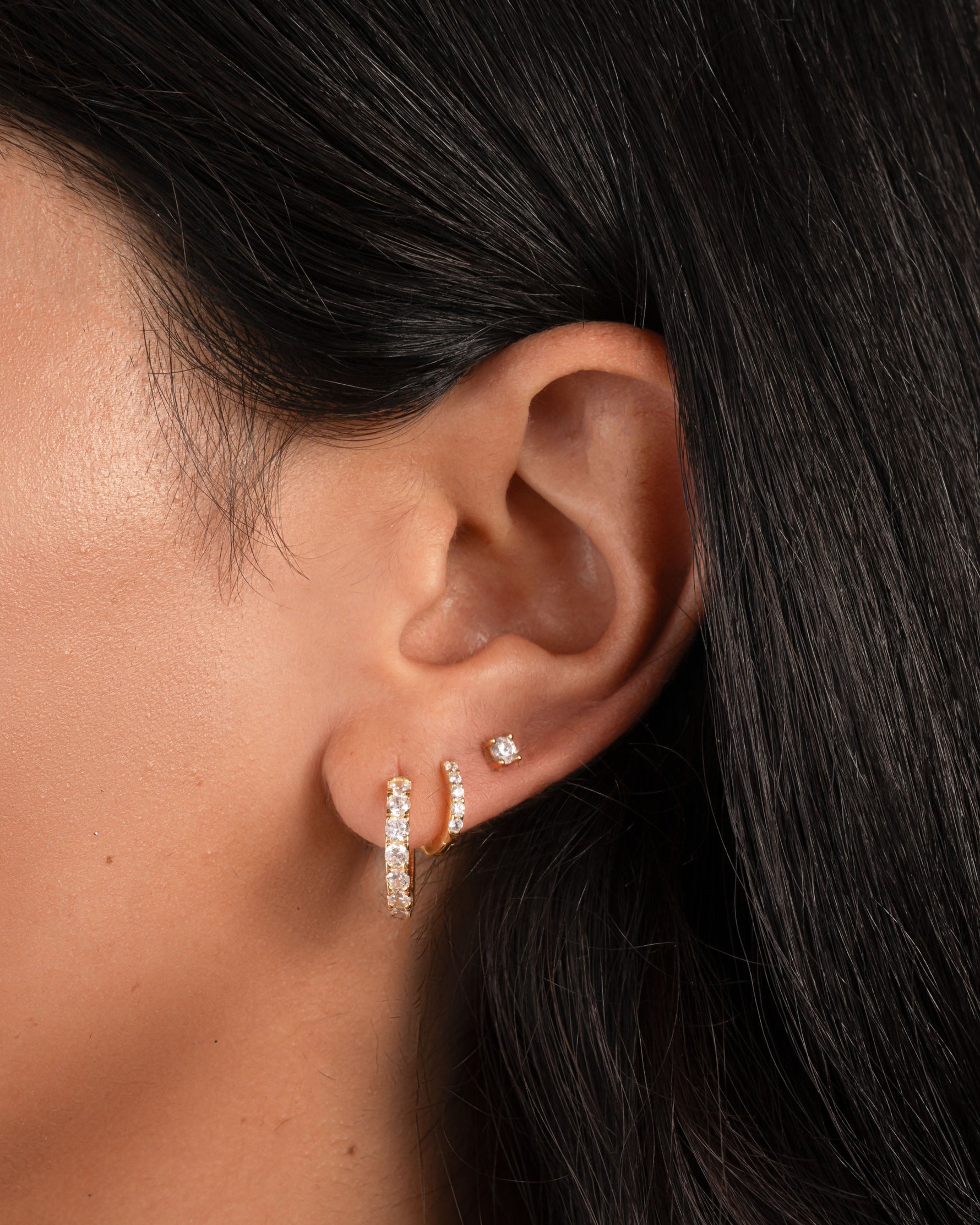 gold cubic zirconia huggie hoop earrings on model, paired with a mini pave hoop earring and a solitaire stud earring