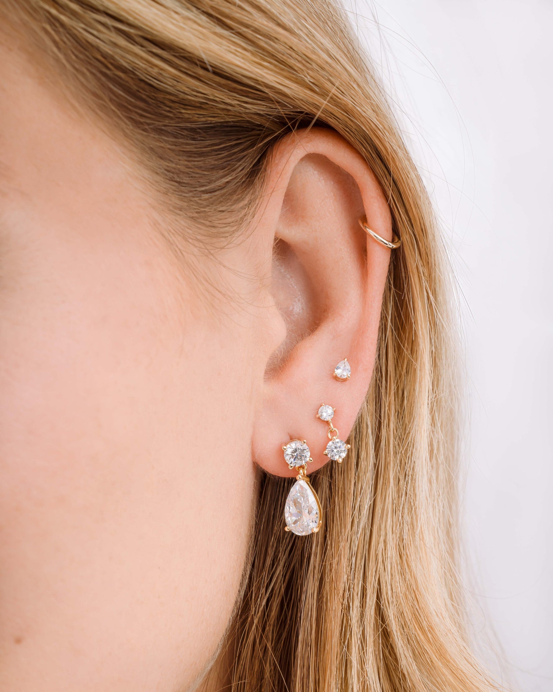 Gold diamond earring stack featuring, elegant earrings with a pear drop design, a charm earring, and a stud earring