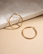 Flatlay of gold textured hoop earrings on neutral background, lightweight hypoallergenic hoops perfect for timeless everyday jewelry.