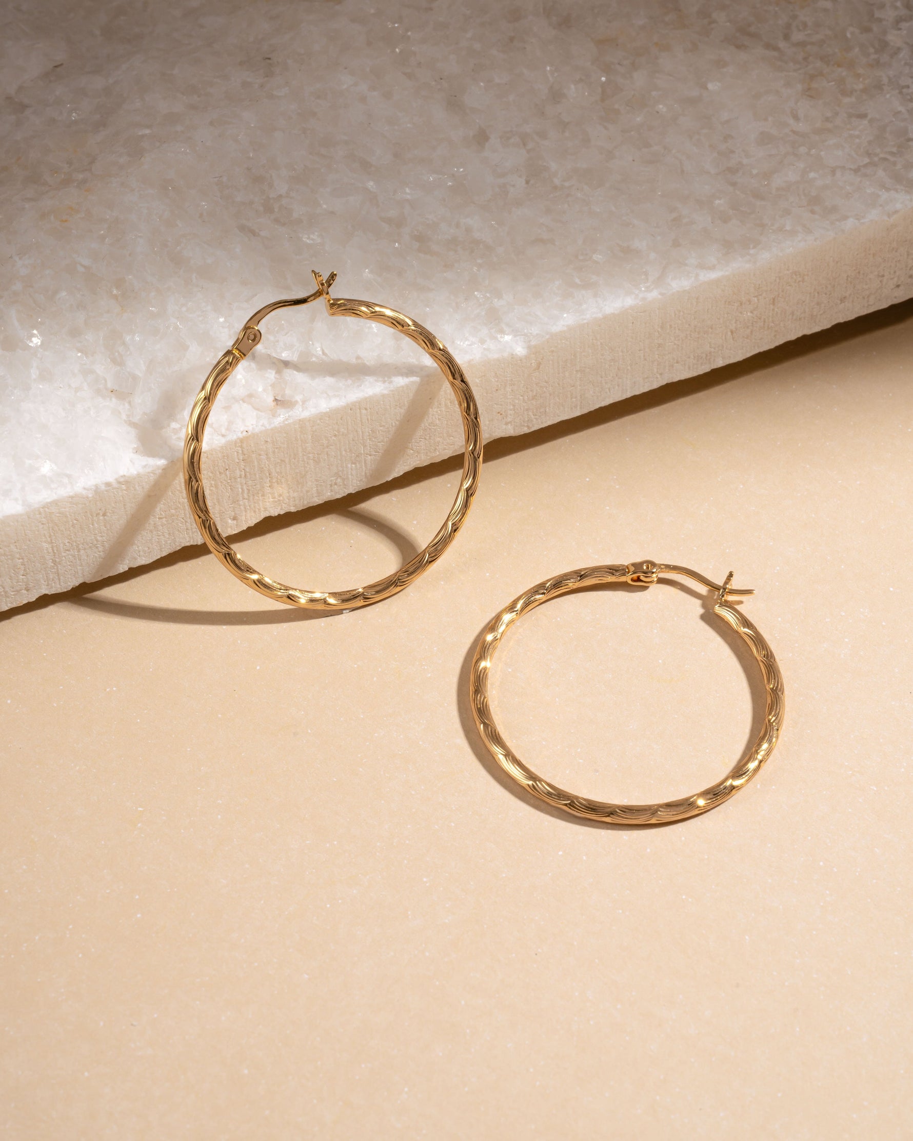Flatlay of gold textured hoop earrings on neutral background, lightweight hypoallergenic hoops perfect for timeless everyday jewelry.