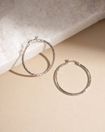 Flatlay of silver textured hoop earrings on neutral background, lightweight hypoallergenic hoops perfect for timeless everyday jewelry.