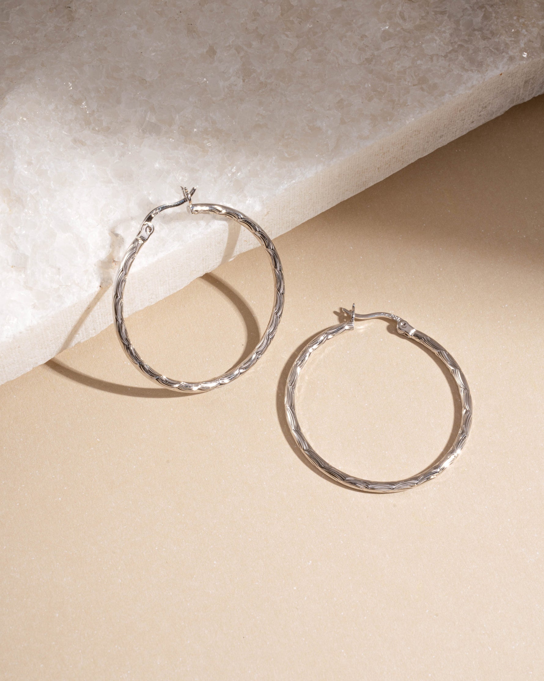 Flatlay of silver textured hoop earrings on neutral background, lightweight hypoallergenic hoops perfect for timeless everyday jewelry.