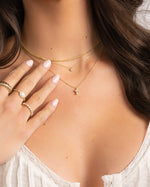 gold necklace stack on model featuring small cross pendant necklace, tiny bezel necklace, and thin rope chain necklace