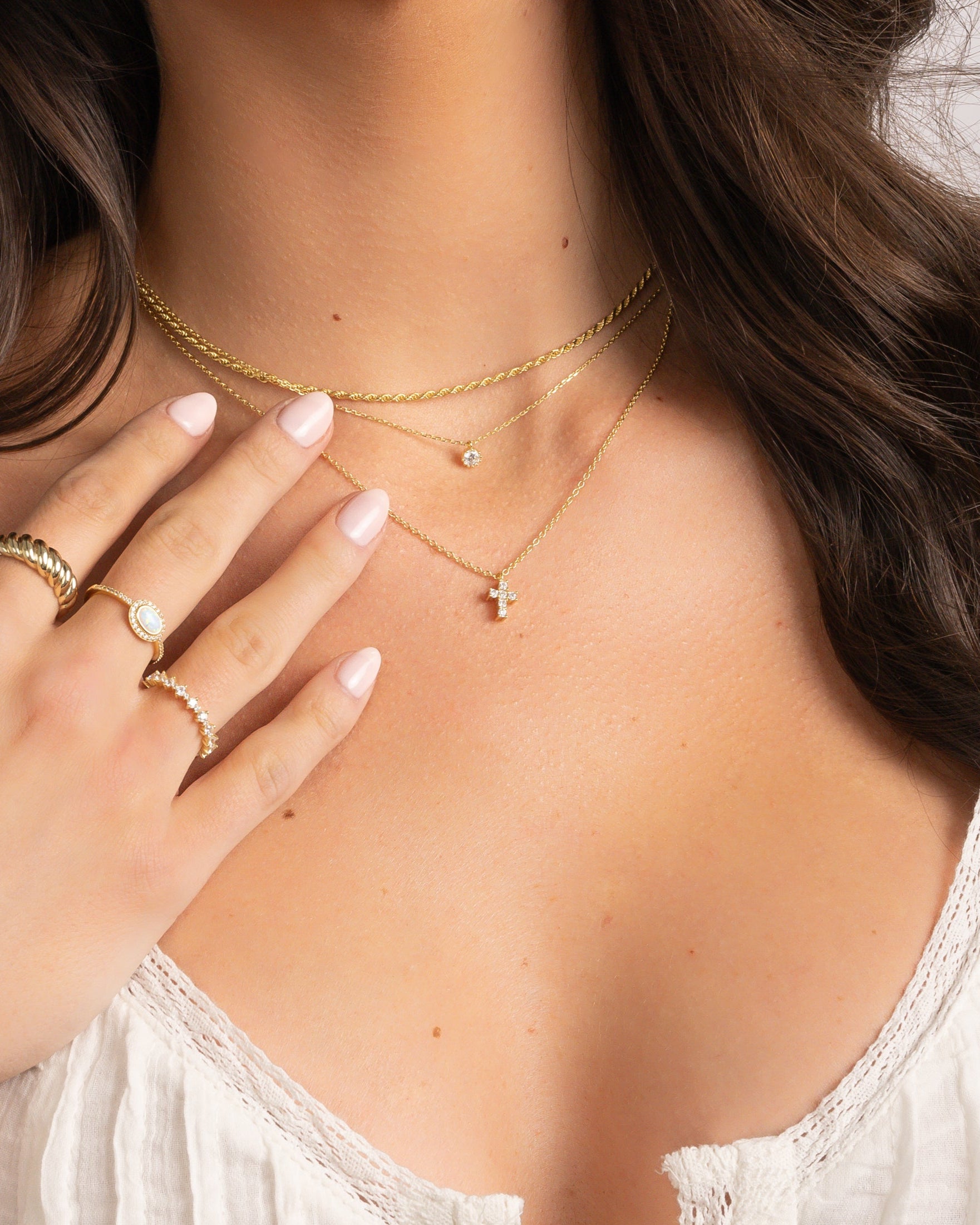gold necklace stack on model featuring small cross pendant necklace, tiny bezel necklace, and thin rope chain necklace