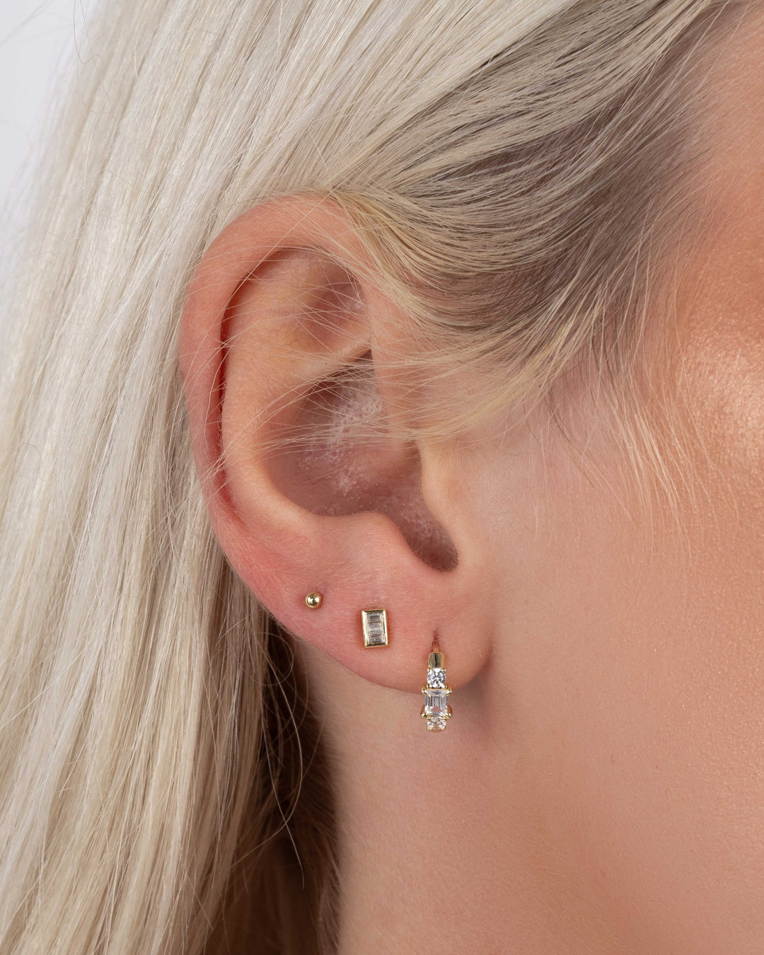 Close-up of a model wearing gold diamond stud earrings, mini gold hoops, and a ball stud