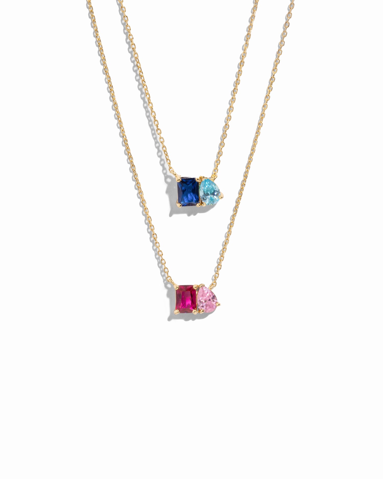 Two gold necklaces with custom birthstone gemstone pendants on a white background, 