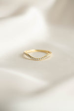 Gold curved ring with small cz diamonds on a light beige fabric background