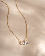 Gold gemstone necklace with cubic zirconia and pearl on a beige background
