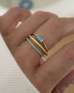 model wearing stackable turquoise rings, featuring a dainty gold band, an eternity band ring with turquoise gemstones and a matching turquoise baguette gemstone ring