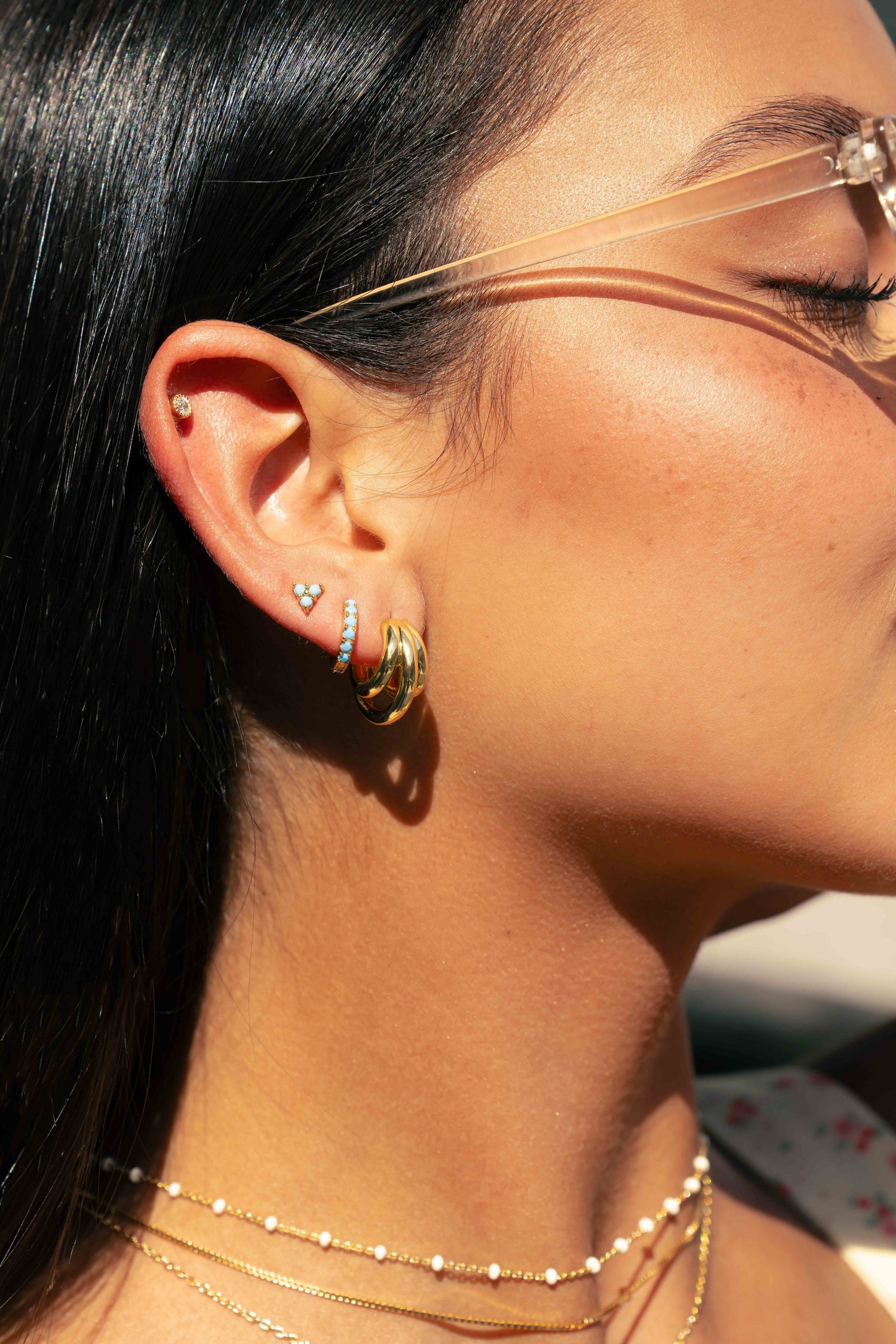 Close-up of model wearing gold hoop earrings paired with turquoise mini hoops and dainty turquoise stud earrings 