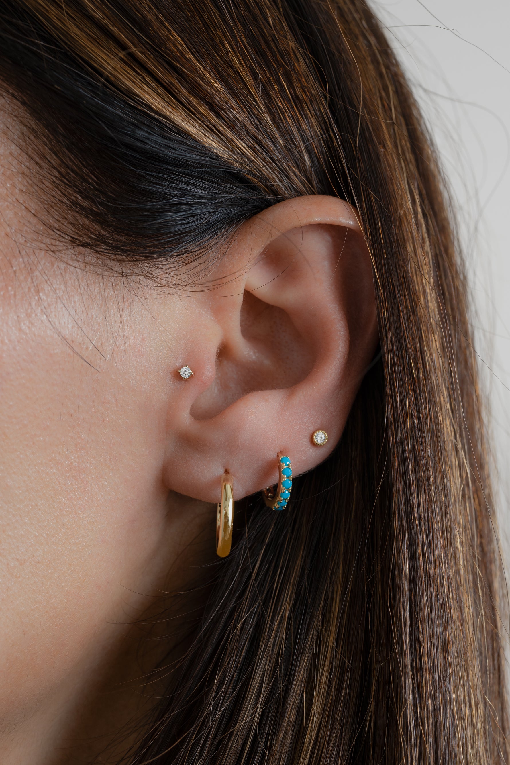 model wearing minimalist gold hoop earrings paired with a small hoop earring with turquoise stones and a tiny stud earring
