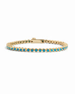 A gold bezel tennis bracelet featuring a continuous row of round turquoise-blue gemstones, displayed on a clean white background.
