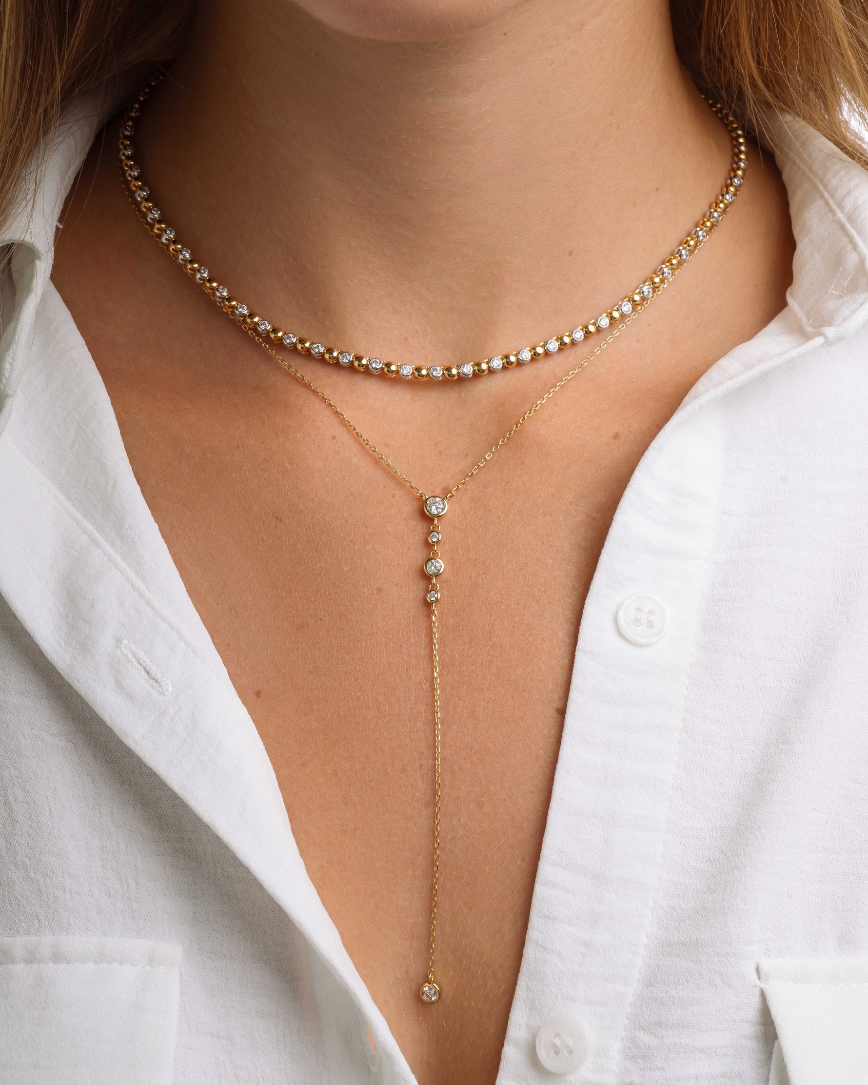 Gold layering necklaces on model featuring a mixed metal jewelry tennis necklace and a bezel set lariat necklace on model