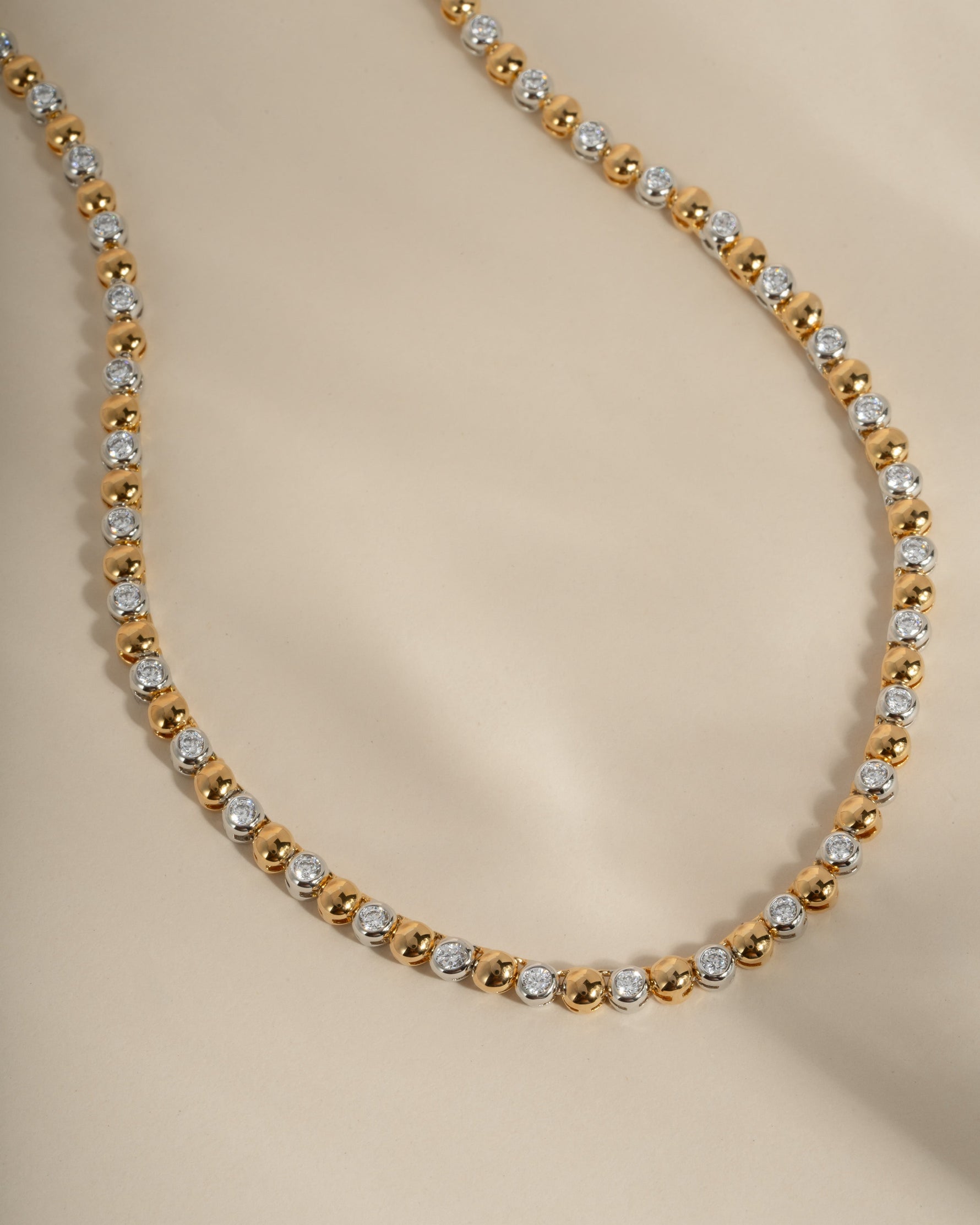 Gold and silver beaded diamond necklace on a beige background