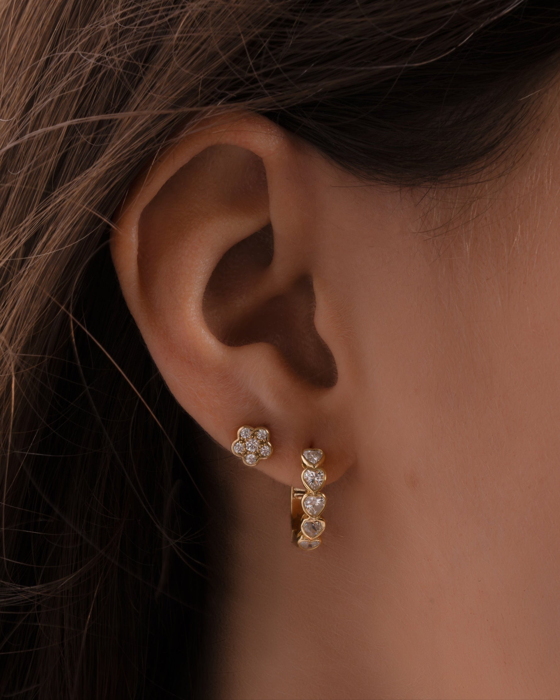 Model wearing a gold heart huggie hoop and a gold flower earring with a cubic zirconia diamonds