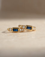 Close-up of Sami Jewels sapphire baguette huggie earrings featuring gold hoops with sparkling blue sapphires.
