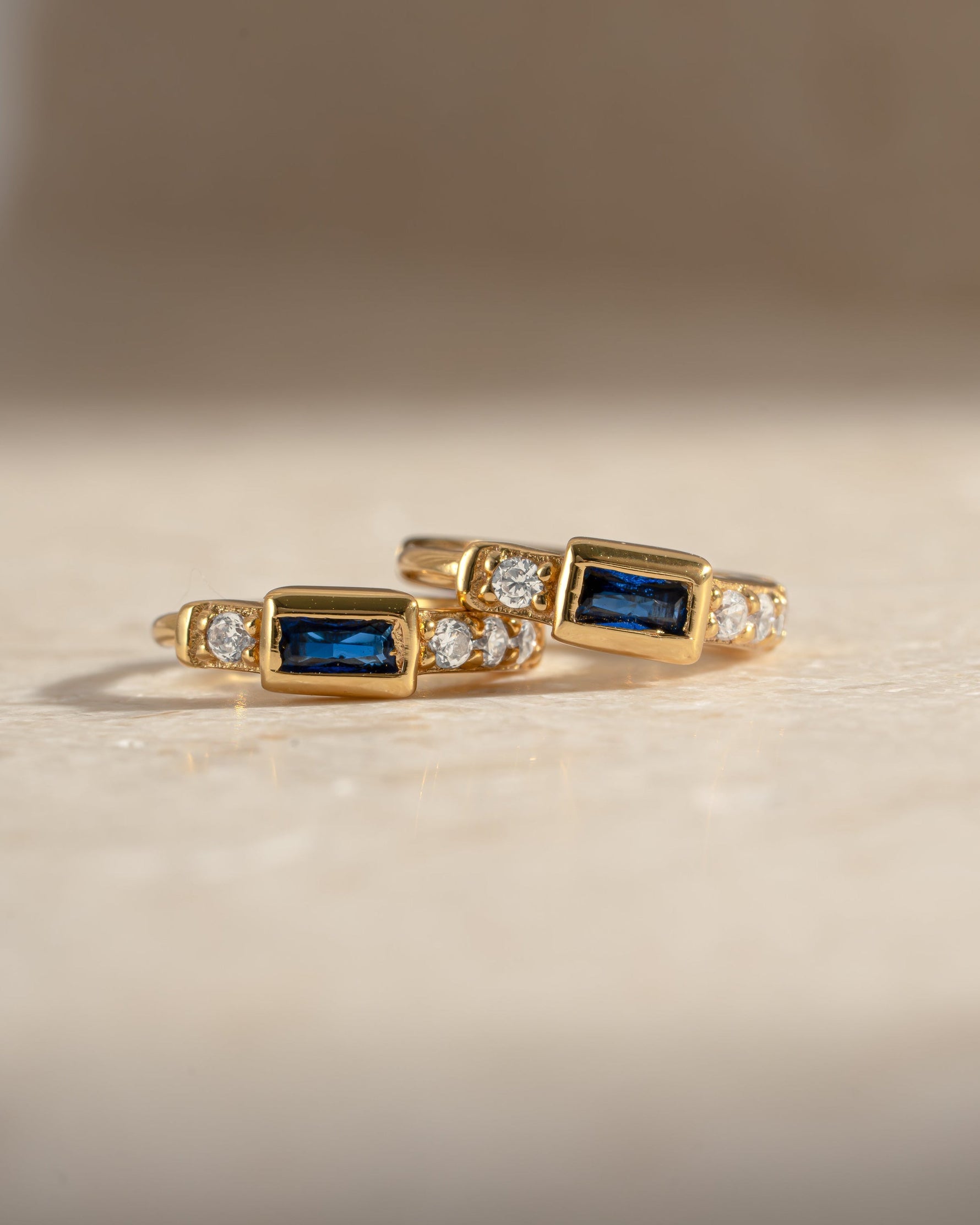 Close-up of Sami Jewels sapphire baguette huggie earrings featuring gold hoops with sparkling blue sapphires.