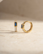 Sapphire Baguette Huggie Earrings by Sami Jewels featuring gold hoops with rectangular blue sapphires.