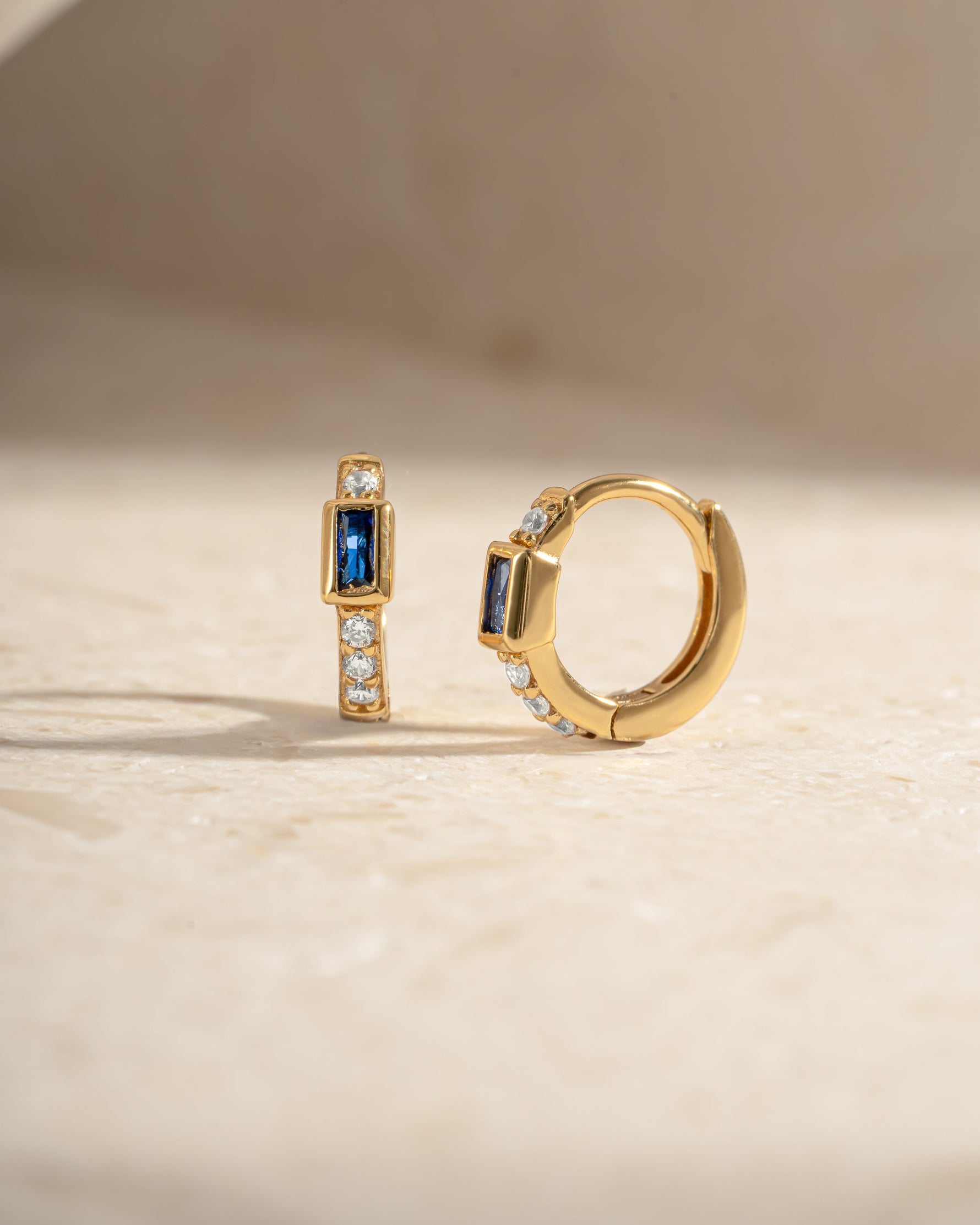 Sapphire Baguette Huggie Earrings by Sami Jewels featuring gold hoops with rectangular blue sapphires.