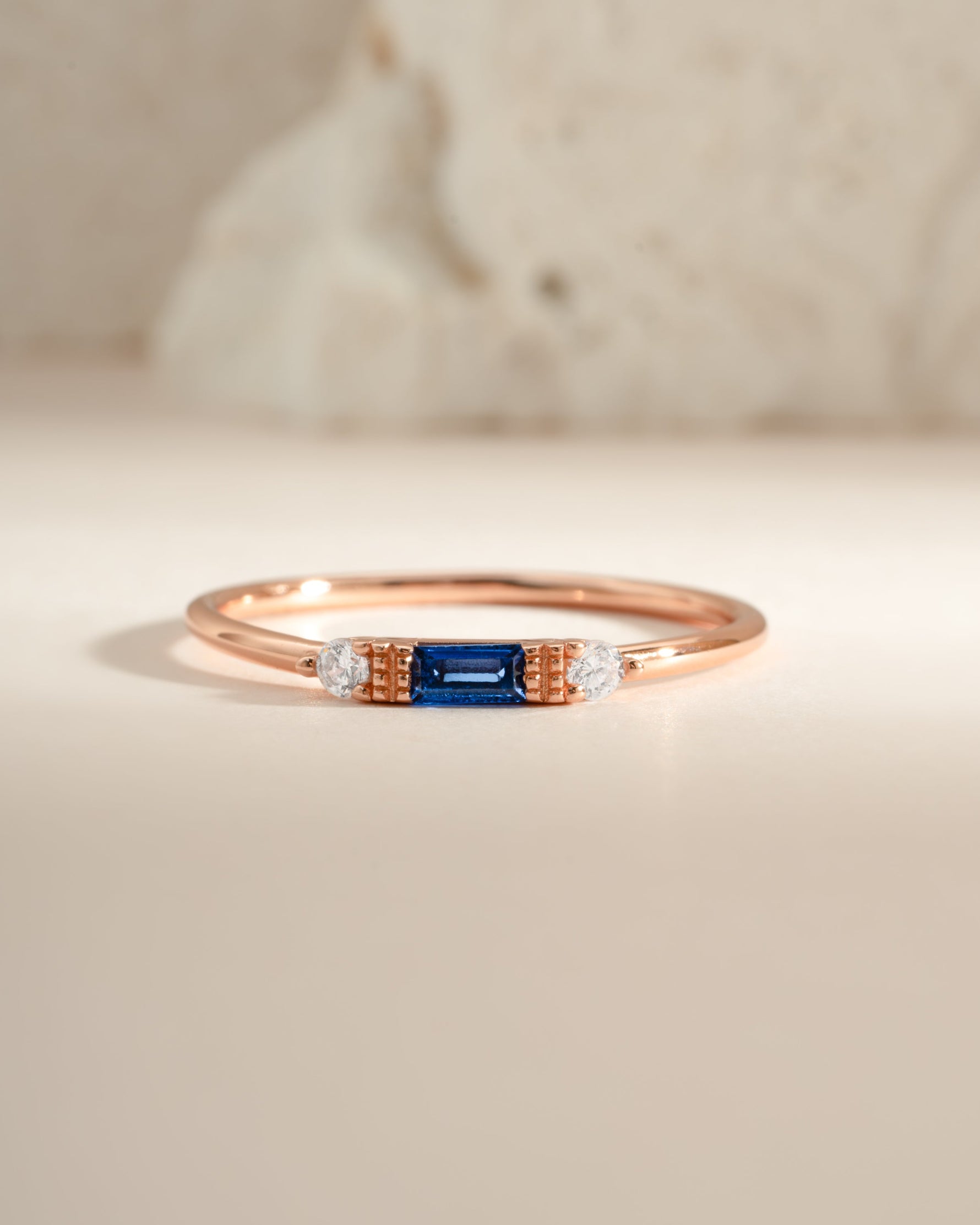 Sami Jewels sapphire baguette ring featuring a rose gold band with a rectangular blue sapphire gemstone.