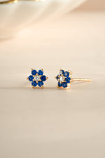Gold sapphire flower stud earrings with a central cubic zirconia stone, featuring a detailed floral design by Sami Jewels.
