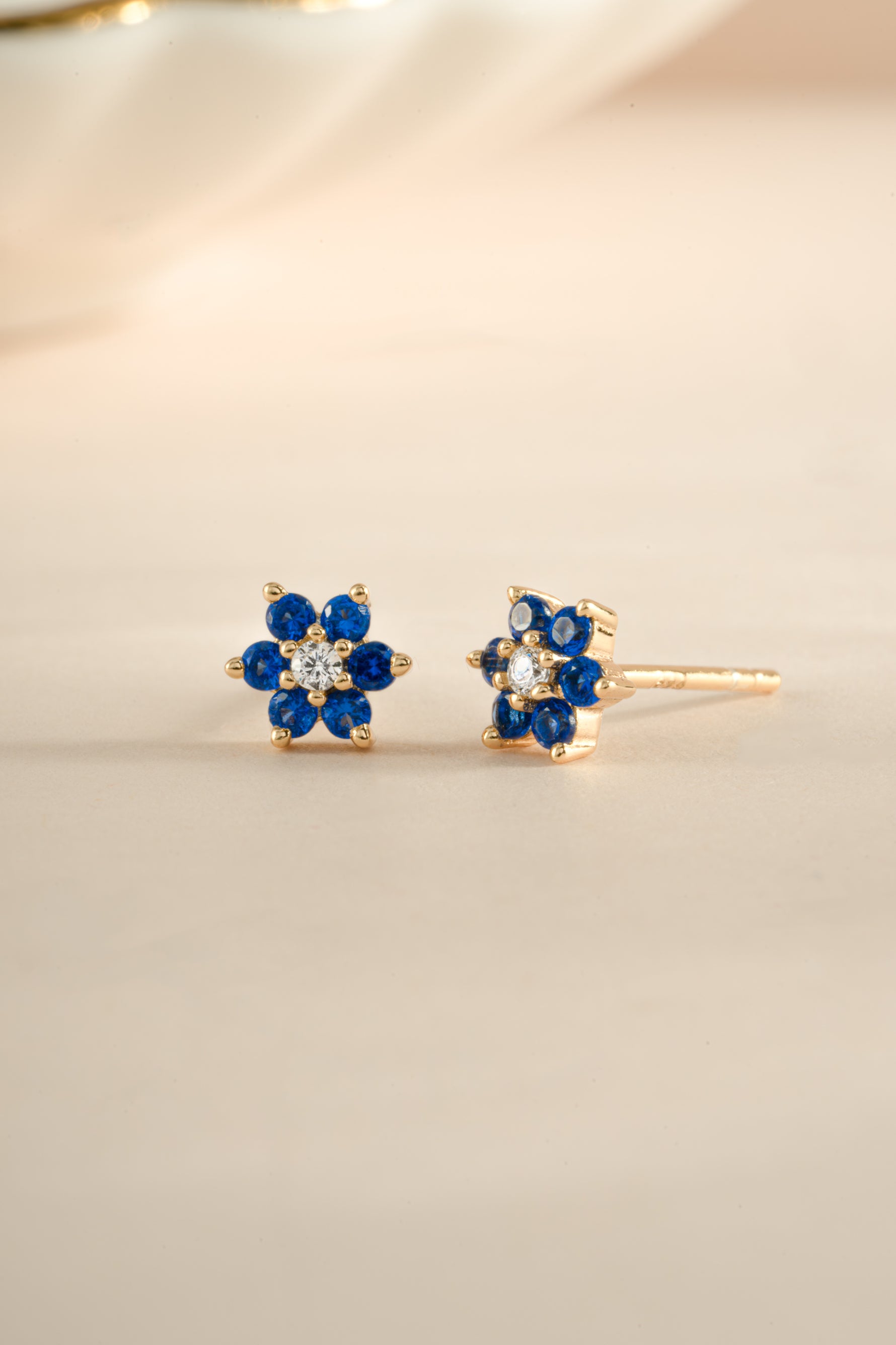 Gold sapphire flower stud earrings with a central cubic zirconia stone, featuring a detailed floral design by Sami Jewels.