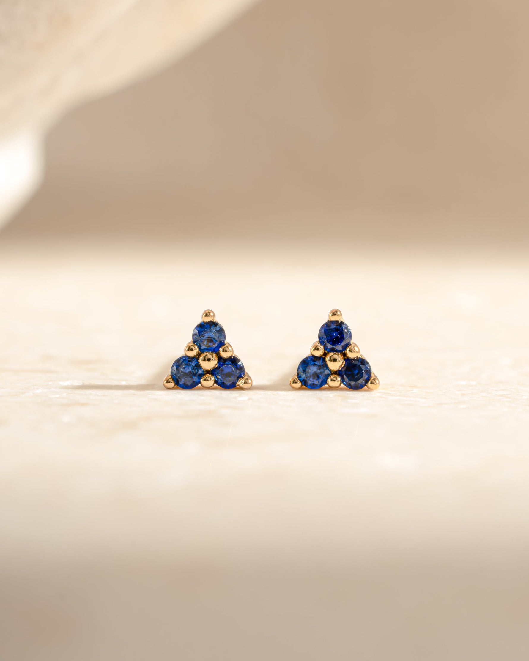 Sami Jewels tiny sapphire three-stone gold earrings, front view showcasing sparkling blue sapphires and gold setting