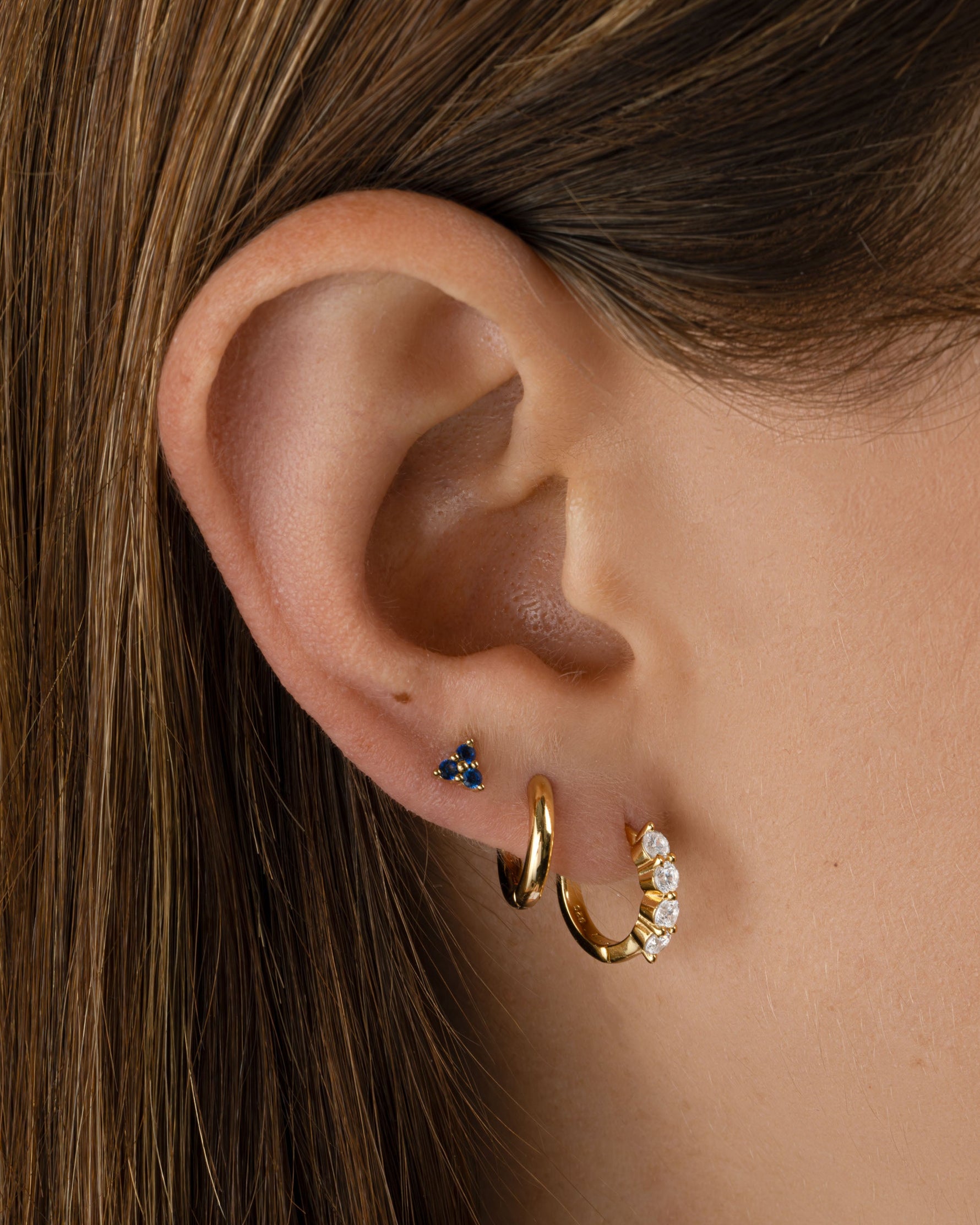 Sami Jewels Tiny Sapphire 3 Stone Stud Earrings featuring small blue sapphires set in gold on a model's ears