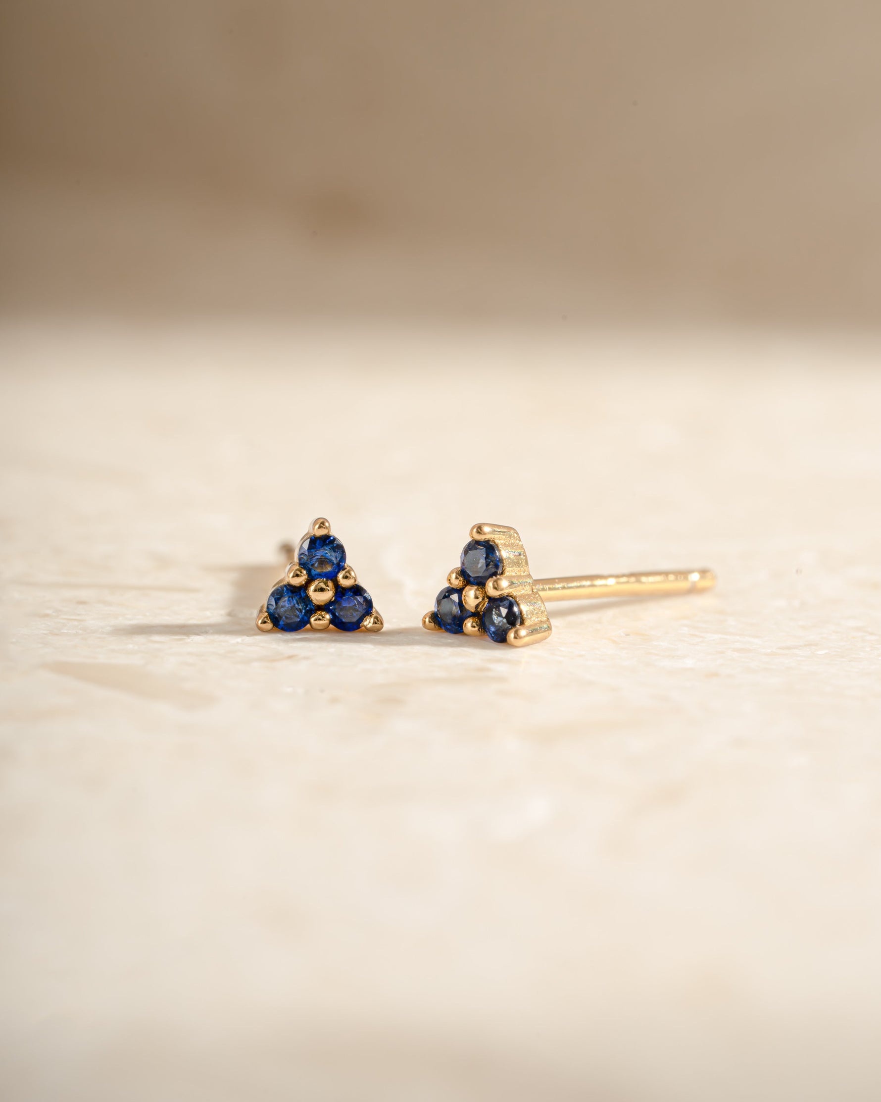 Sami Jewels tiny sapphire three-stone stud earrings with gold settings, showcasing sparkling blue sapphires and a sleek design.