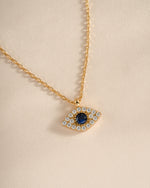 Gold Sapphire Evil Eye Necklace by Sami Jewels featuring a detailed sapphire charm and intricate gold chain.