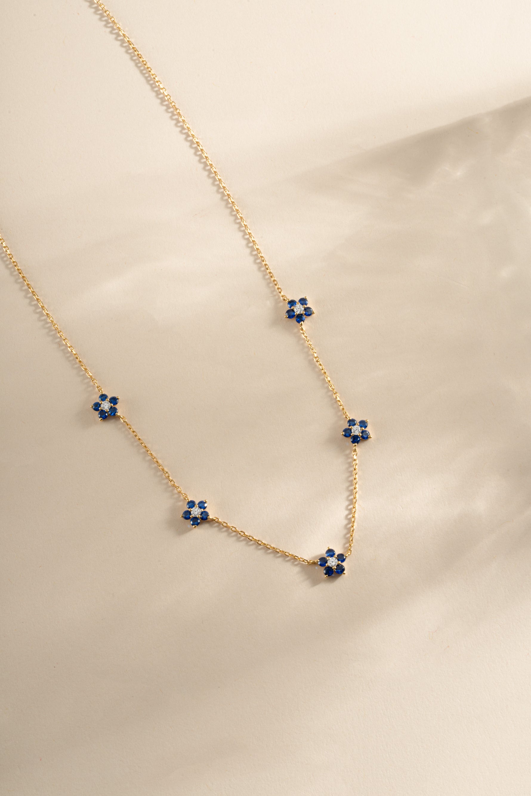 Gold sapphire flower necklace featuring a delicate sapphire flower charm, designed by SJ Faire.