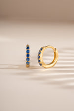 Gold 7mm sapphire-studded huggie earrings by Sami Jewels, showcasing elegant sapphire accents on small hoop earrings.