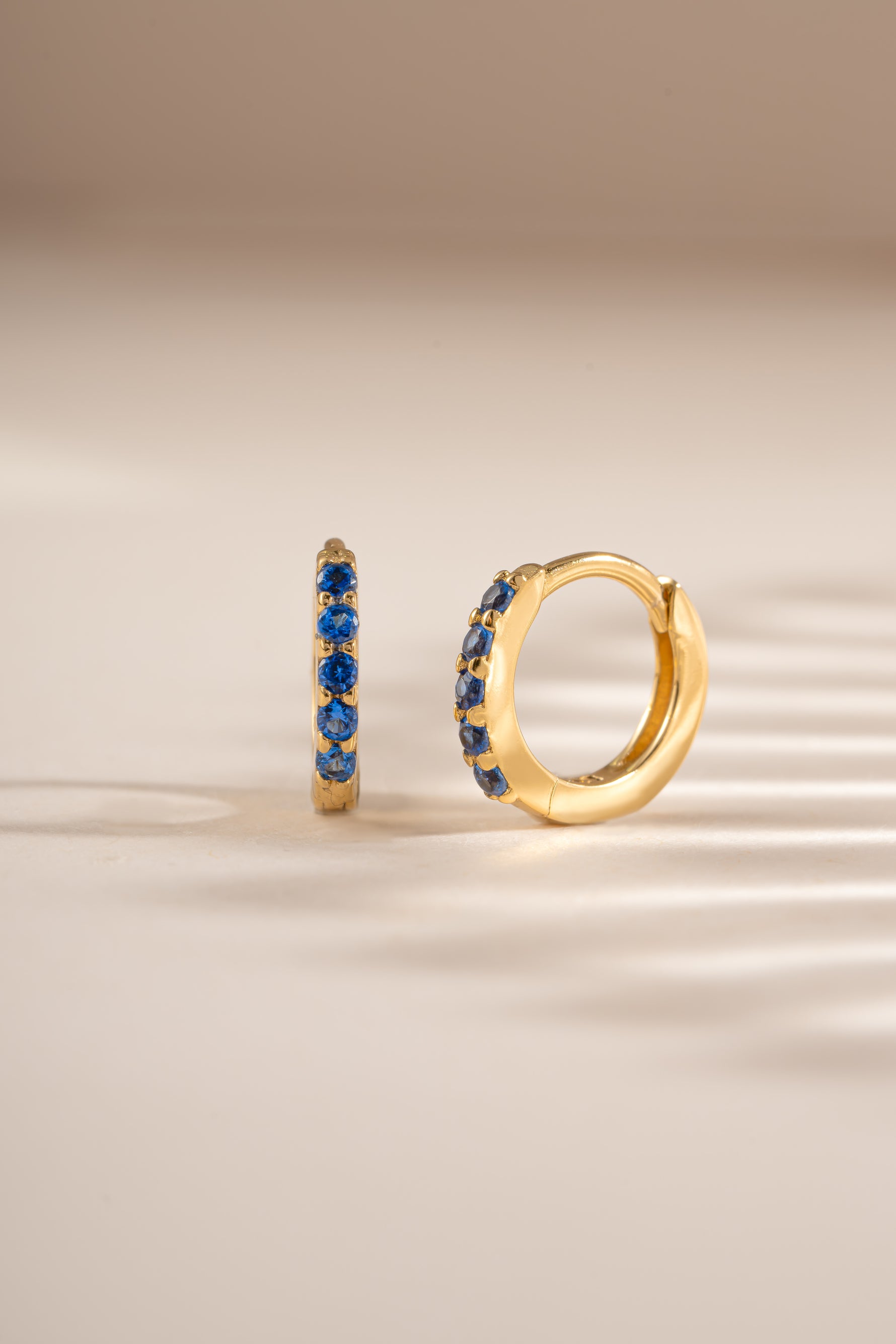 Gold 7mm sapphire-studded huggie earrings by Sami Jewels, showcasing elegant sapphire accents on small hoop earrings.