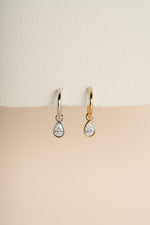 Gold and silver pear CZ charm earrings side by side against a warm neutral background.
