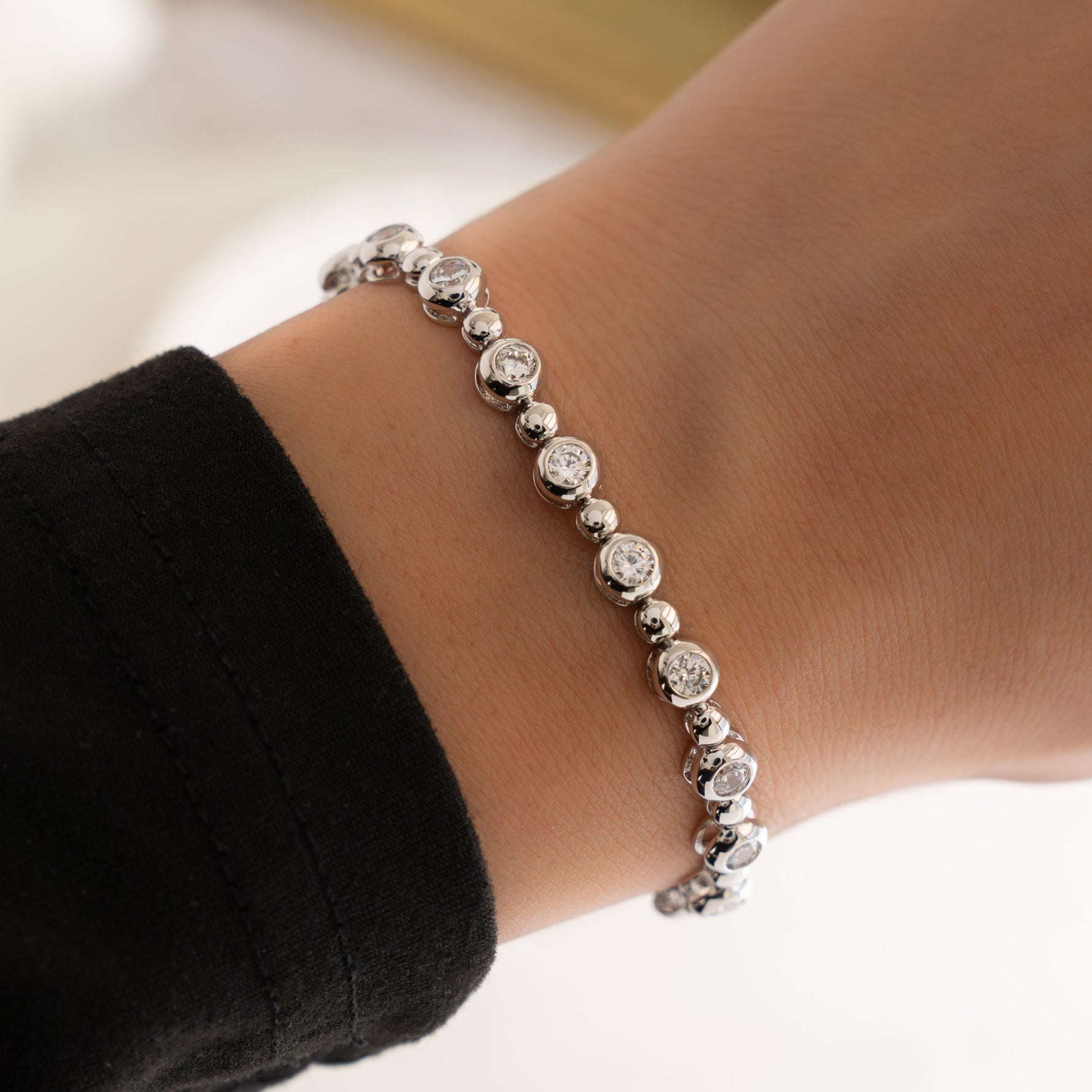 Close-up of a dainty silver bracelet with diamond gems, worn by the model