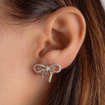 Model wearing sterling silver stud earrings, bow-shaped with a smooth finish, ideal for layering with other jewelry.