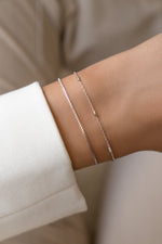 Silver box chain and satellite bracelets worn together on a model's wrist.