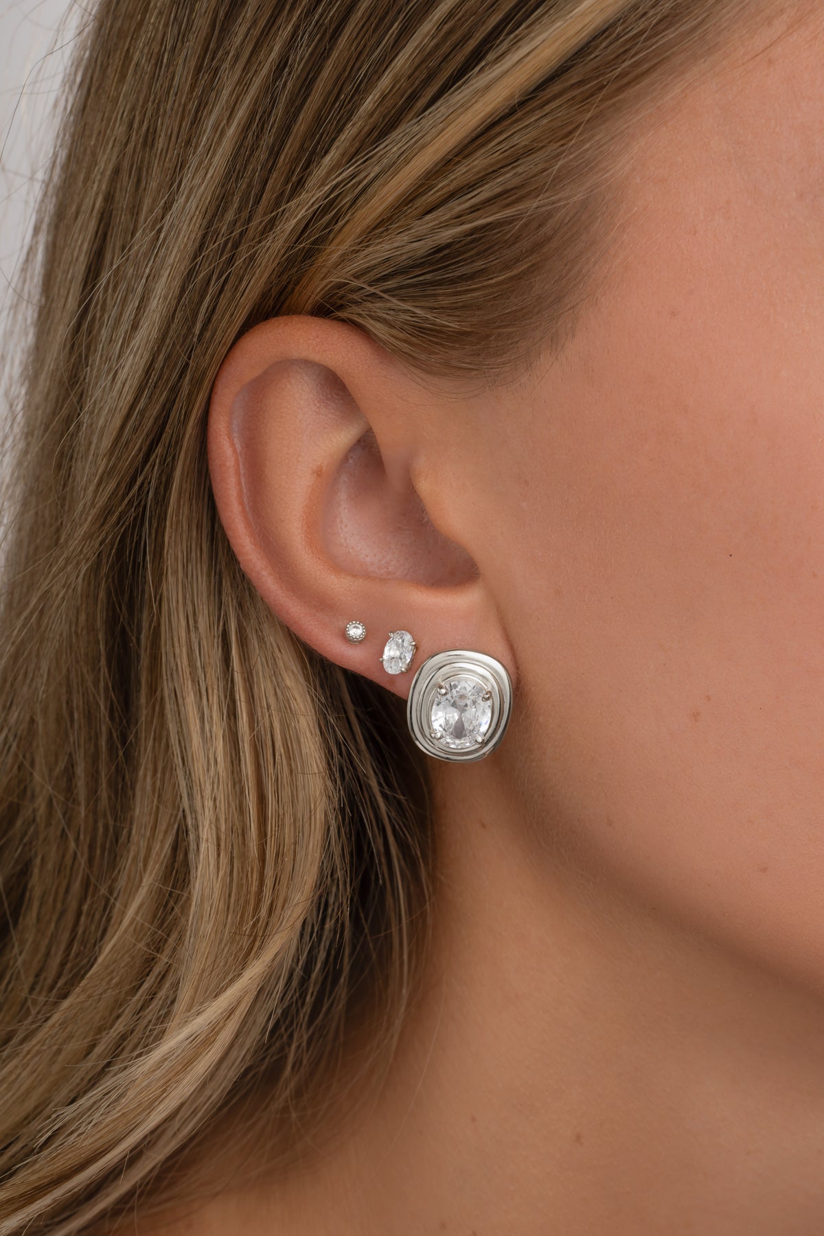 Close-up of a silver oval bezel statement stud on an ear, with smaller oval and round studs.