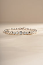 Silver graduated bezel tennis bracelet arranged on a cream background.