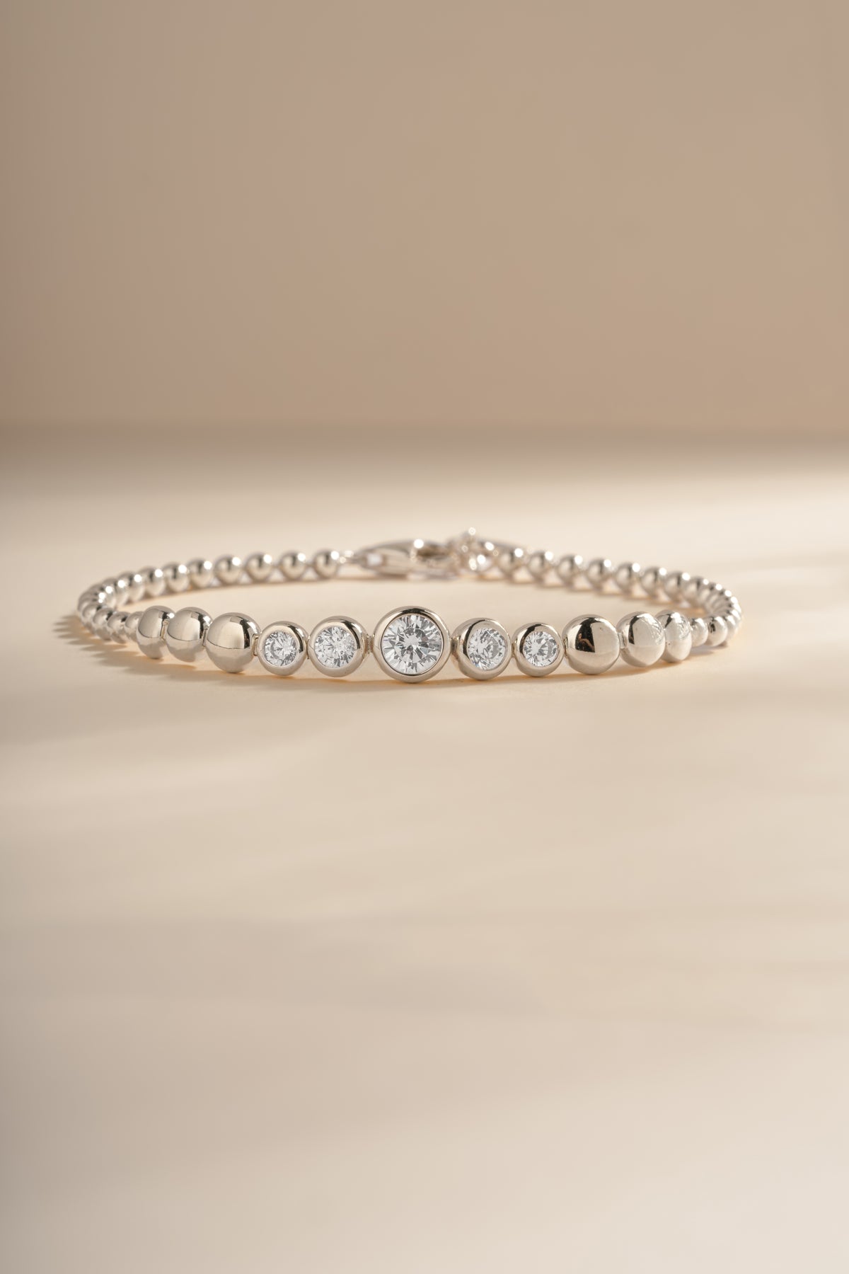 Silver graduated bezel tennis bracelet arranged on a cream background.