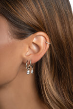 Silver pear CZ charm huggie on a model's ear, styled with a marquise charm hoop and a slim ear cuff.