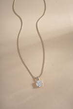 Silver round solitaire pendant and chain arranged on a cream background.