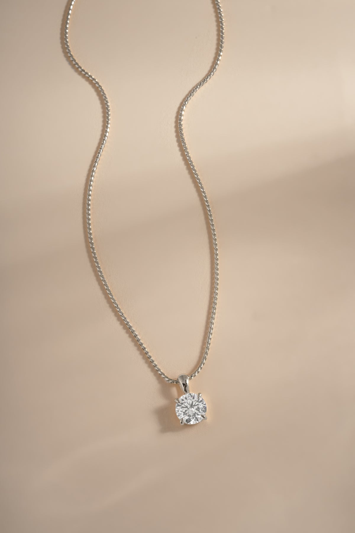 Silver round solitaire pendant and chain arranged on a cream background.
