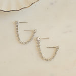 close up of silver earrings with double piercing diamond tennis chain.