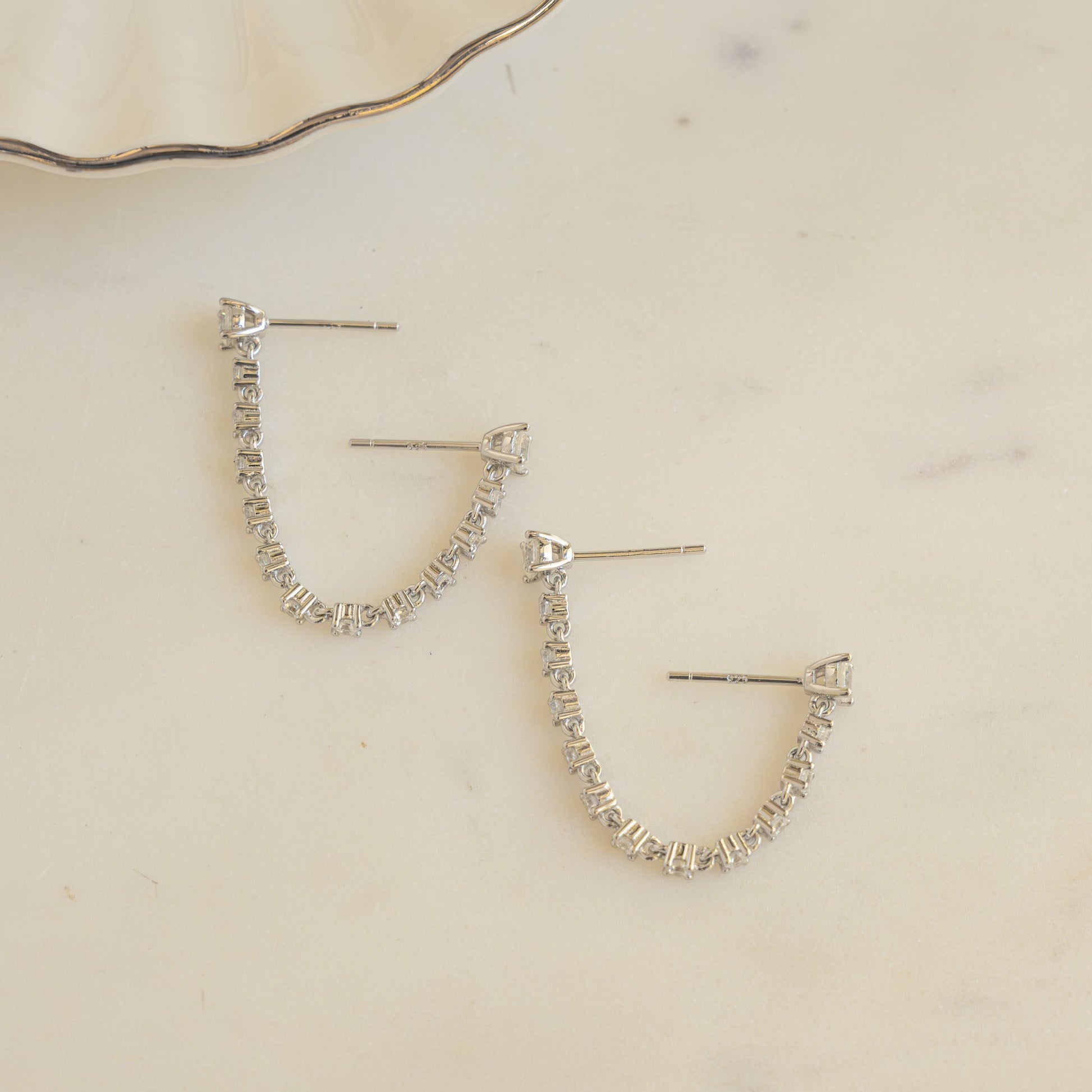 close up of silver earrings with double piercing diamond tennis chain.