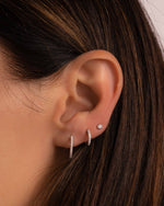 model wearing minimalist pave huggie earrings in two different sizes and a diamond bezel stud earring in sterling silver 