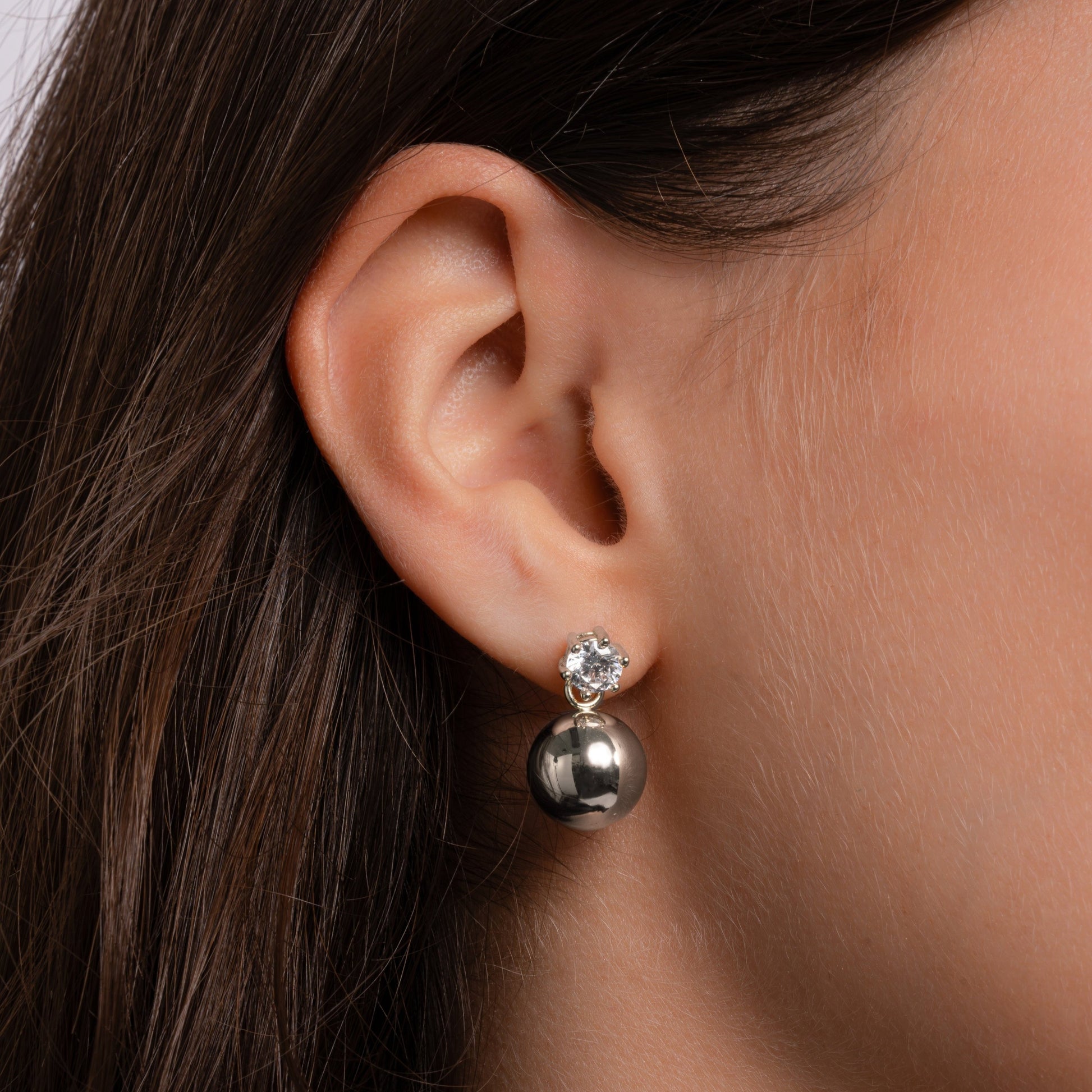 Model wearing small silver earrings with a ball and delicate diamond design.