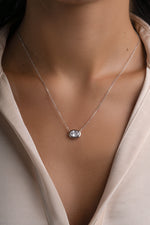 Silver east-west oval bezel pendant worn alone on a model in a white shirt.